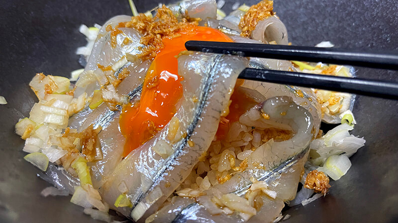 卵黄とサヨリ刺身を箸で持ち上げた丼の接写