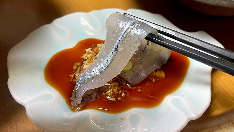 生姜醤油につけたサヨリ刺身を箸で持ち上げた写真
