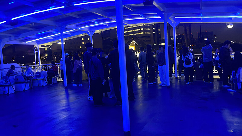 青い照明に包まれた夜のデッキに集まる乗船客