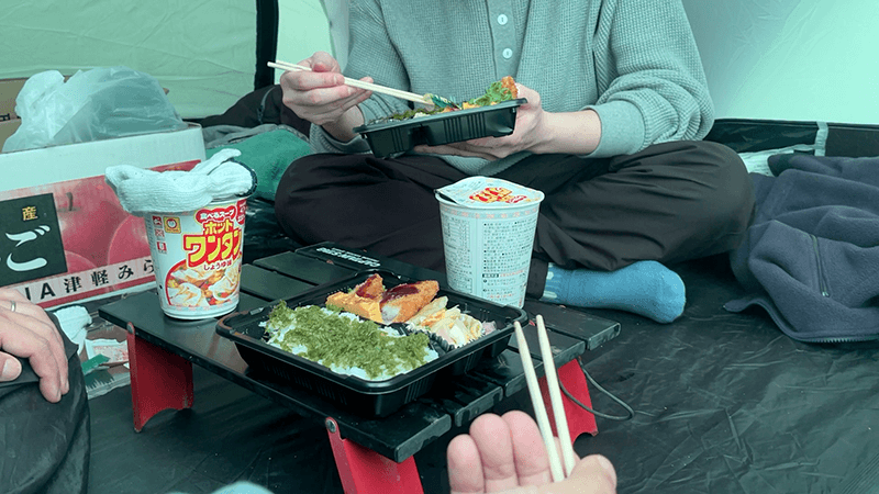 カップ麺とのり弁を広げて安堵するテント内の昼食