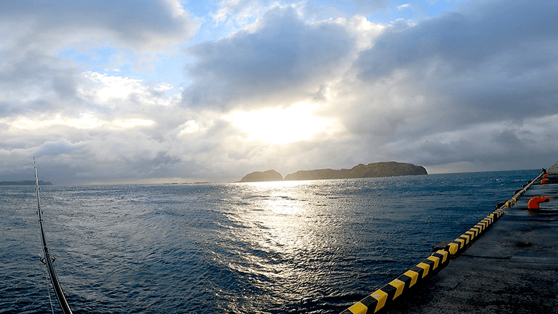雲の切れ間から光が差す新島港の夕方の海