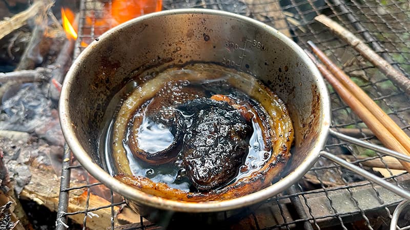 香ばしく焼いたウナギの背骨と頭をタレで煮る様子