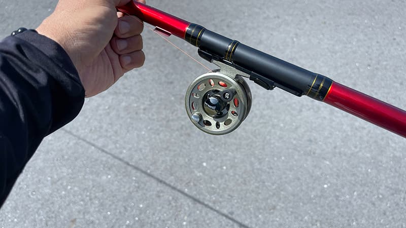 赤いヘチ竿と太鼓リールを手に持ったヘチ釣りのタックル