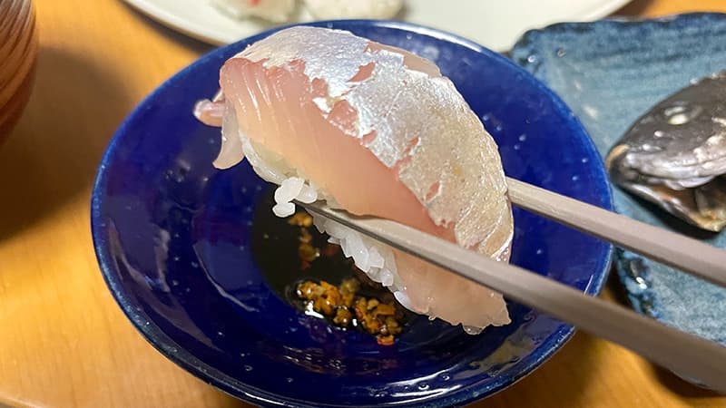 薬味を落とした醤油にシマアジの握りをつける箸先