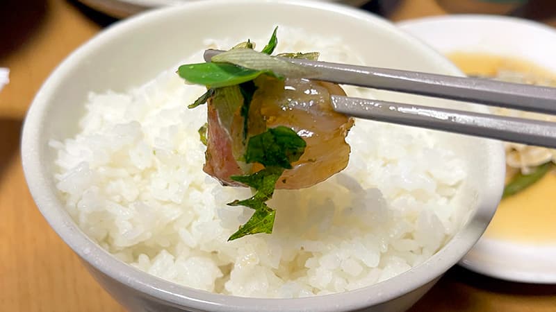 白いご飯に薬味を和えたスズキの身を箸でのせる漬け丼