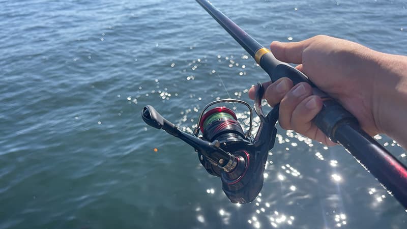 光る海面に向けて構えた磯竿と、レバーブレーキ付きのリールを握る手