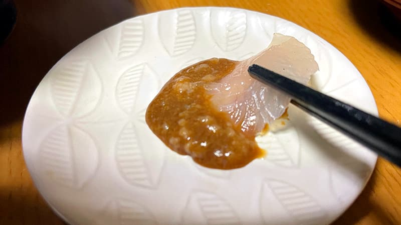 肝醤油をたっぷりと絡めたカワハギの刺身を箸で持ち上げたところ